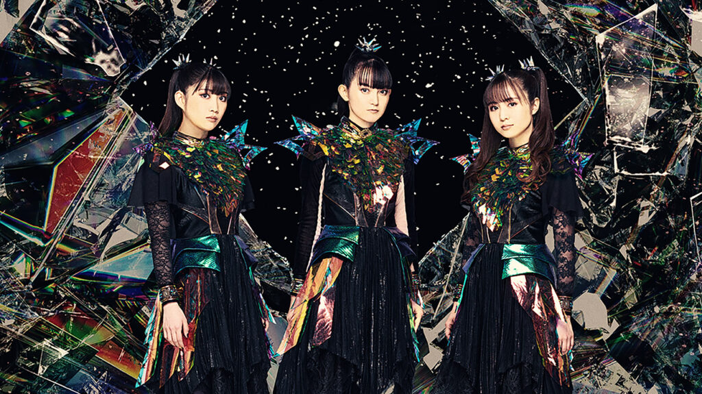 BABYMETAL band members in striking black and blue outfits stand in front of a fractured mirror.