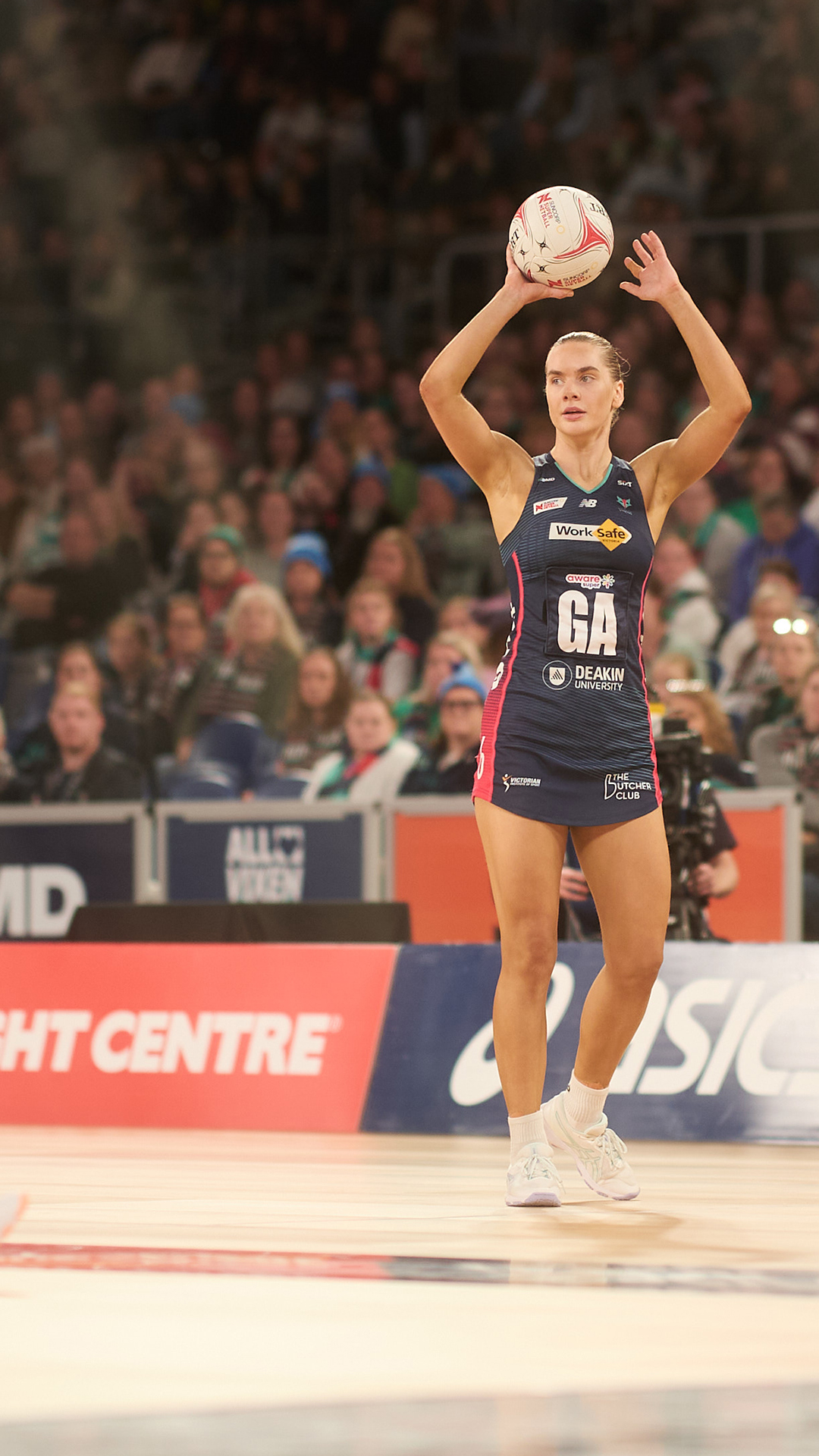 Netballers in action in a packed stadium.