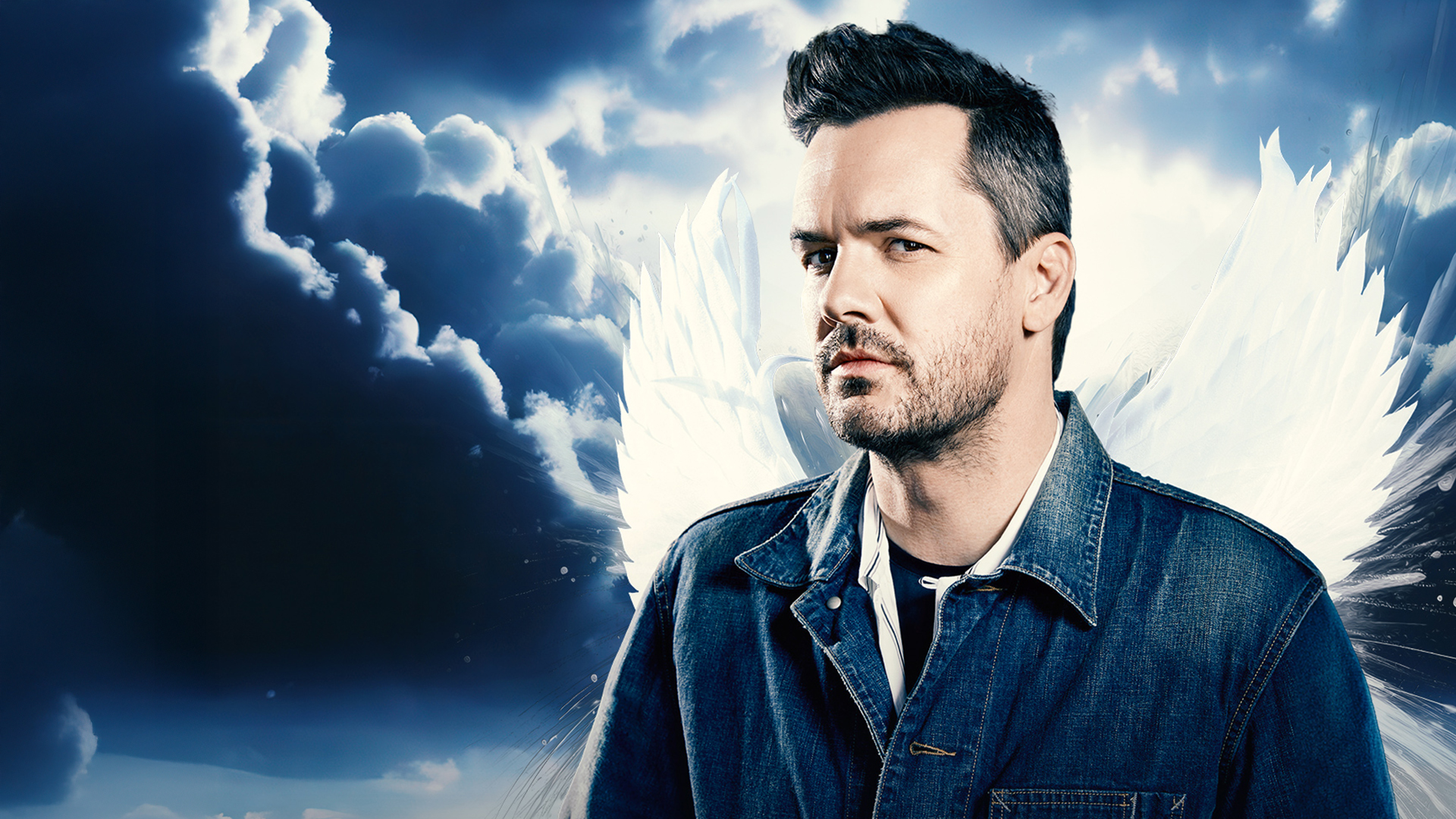 Jim Jefferies with angel wings posing against a clouded background.