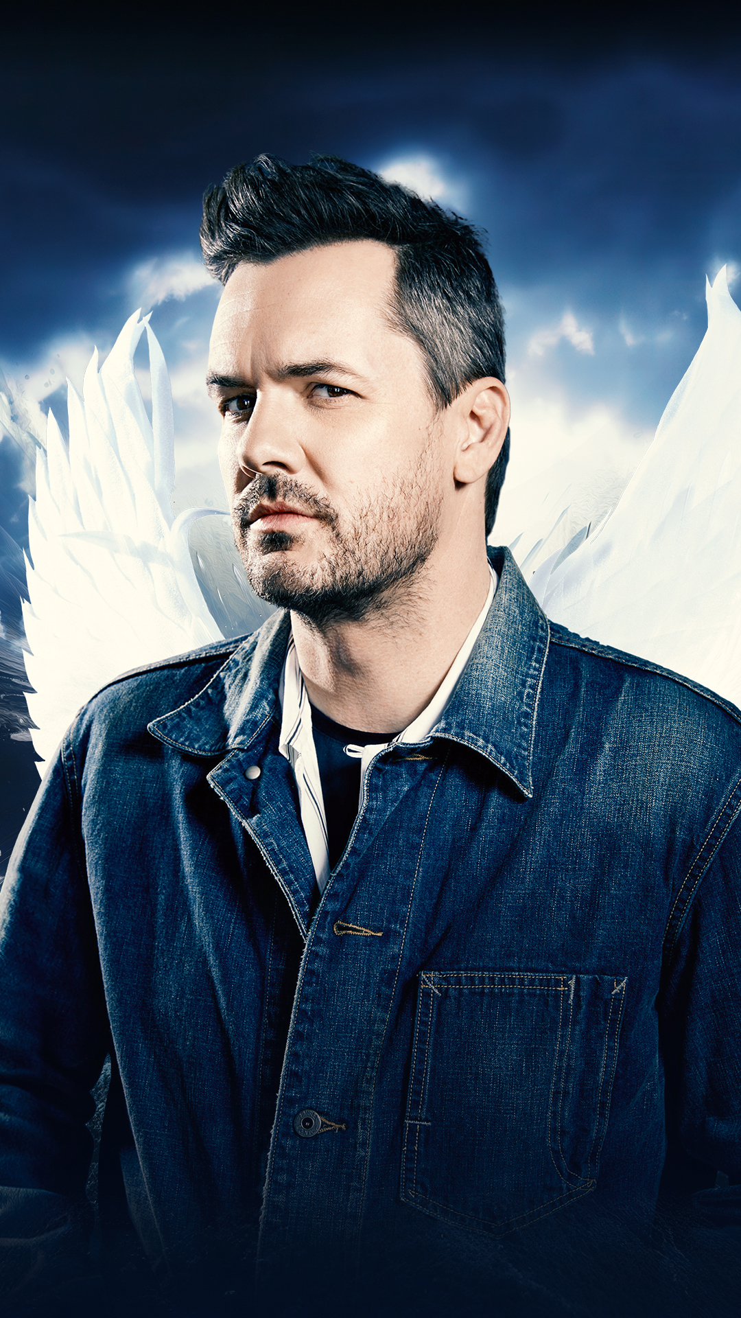 Jim Jefferies with angel wings posing against a clouded background.