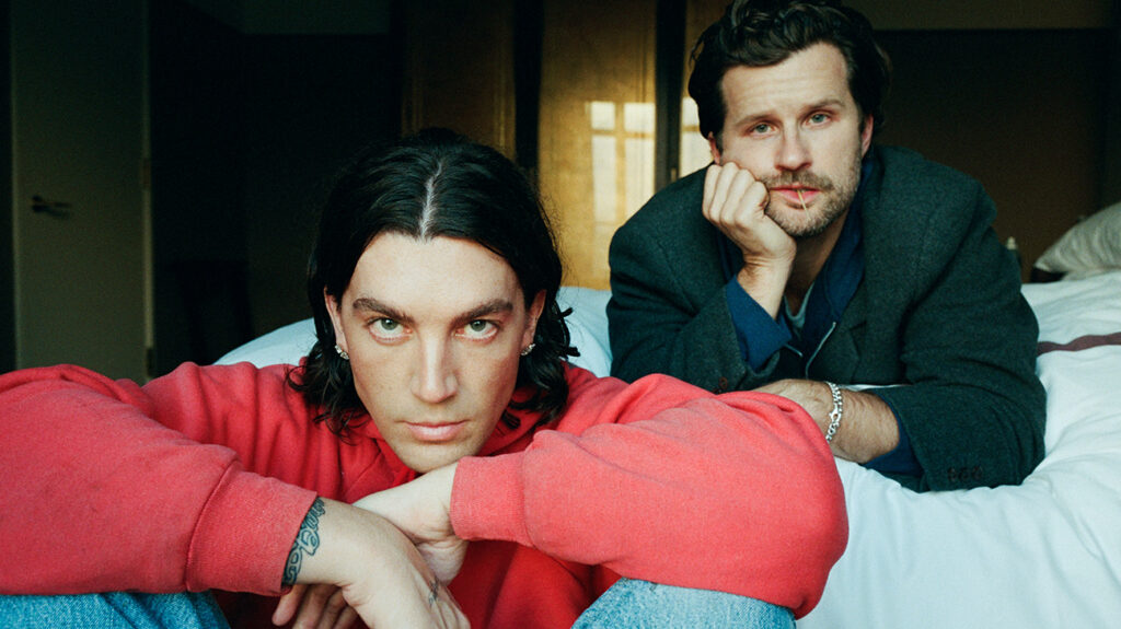 LANY band members sitting on a bed with serious poses.