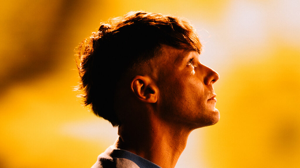 Louis Tomlinson, sporting short hair and a blue shirt, poses confidently for the photograph.