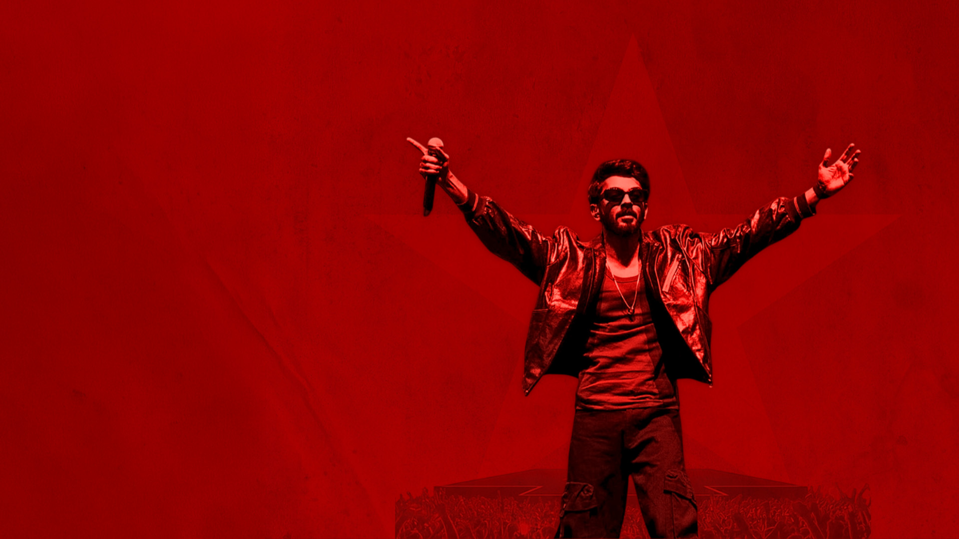 Singer Anirudh with microphone in hand and arms in the air against a red background.