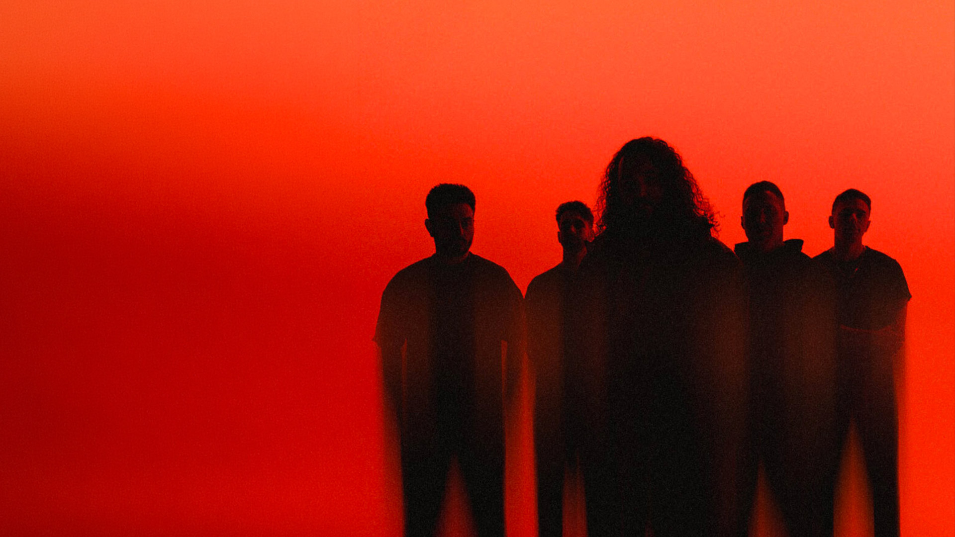 Five band members in shadows in front of a red background.