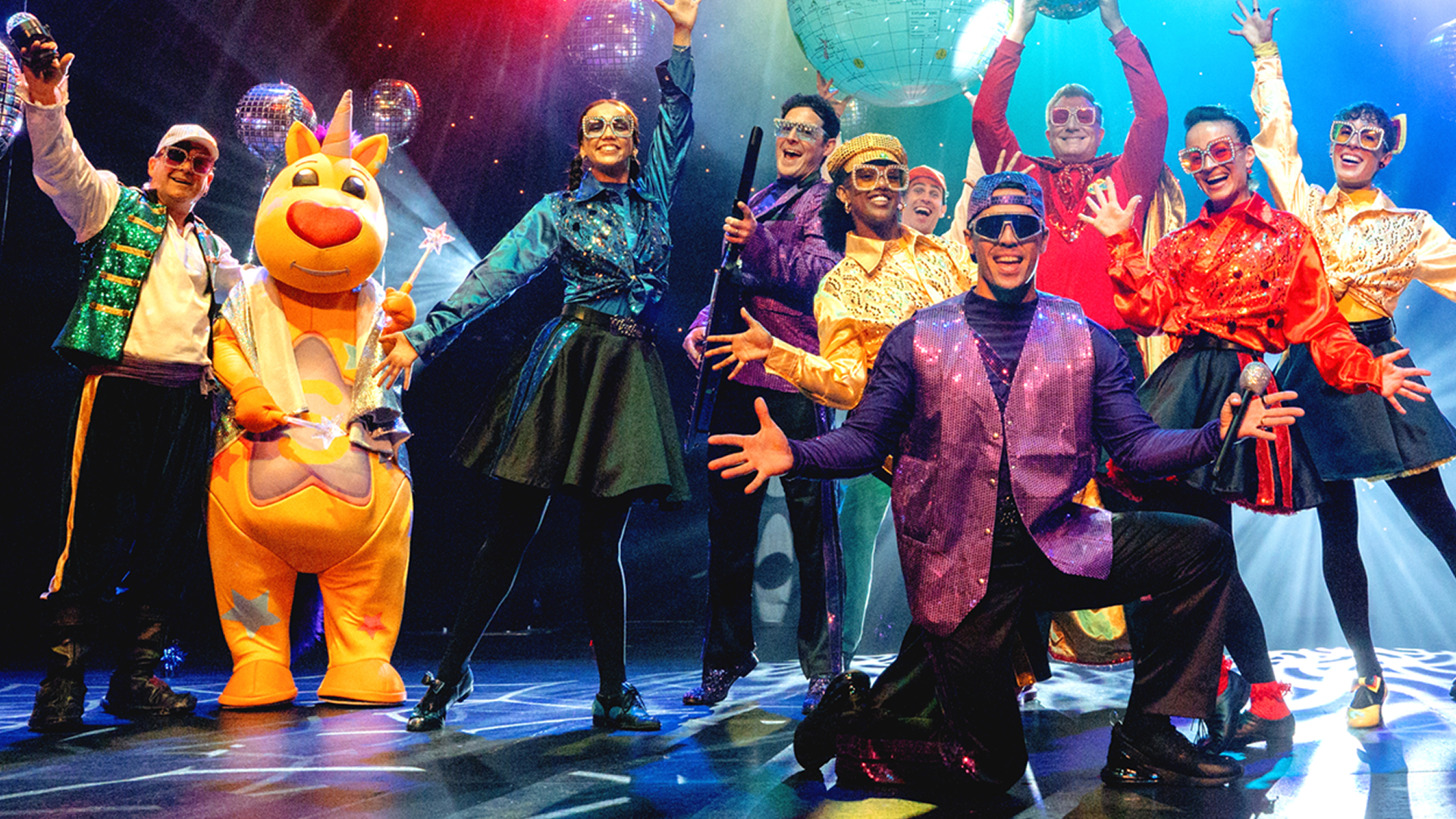 The Wiggles in colorful costumes on stage, entertaining an audience with music and dance.