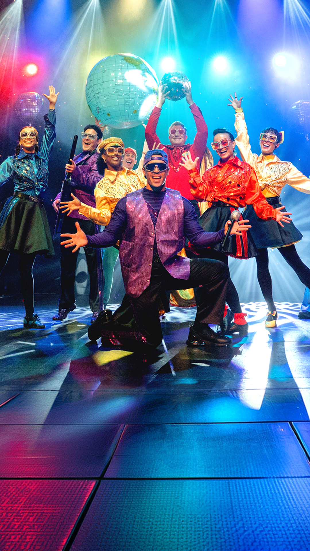 The Wiggles in colorful costumes on stage, entertaining an audience with music and dance.
