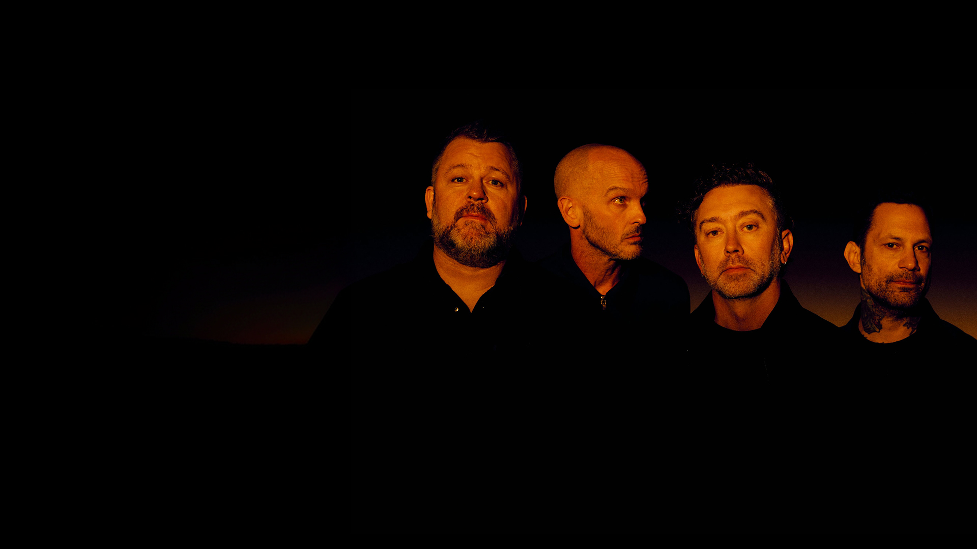 Rise Against band members band pose together in front of a solid black background.