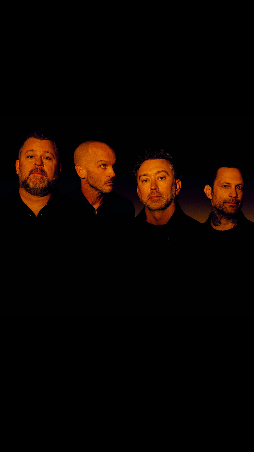 Rise Against band members band pose together in front of a solid black background.